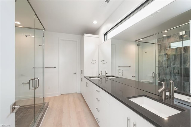 bathroom featuring a sink, double vanity, a shower stall, and wood finished floors