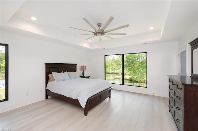 bedroom featuring a tray ceiling, light wood-type flooring, and multiple windows