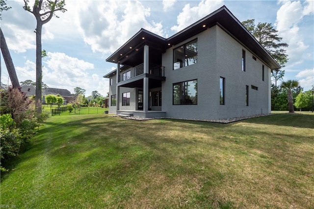 back of property with a balcony, brick siding, fence, and a lawn