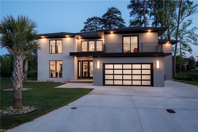 modern home featuring an attached garage, concrete driveway, a front lawn, a balcony, and brick siding