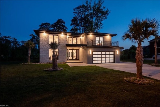 view of front facade featuring french doors, a balcony, concrete driveway, a garage, and a lawn