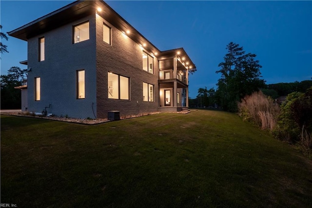 back of house at night featuring brick siding, a lawn, and a balcony