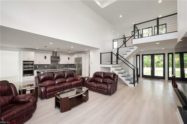 living room with light wood-type flooring, stairway, french doors, and a high ceiling