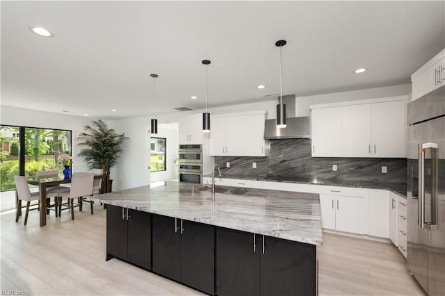 kitchen featuring stainless steel appliances, wall chimney range hood, backsplash, and light wood-type flooring