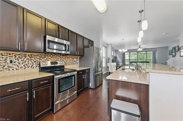 kitchen featuring stainless steel appliances, a sink, a kitchen island with sink, dark brown cabinets, and pendant lighting