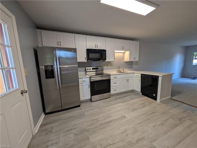 kitchen with light wood-style flooring, a sink, a peninsula, black appliances, and light countertops