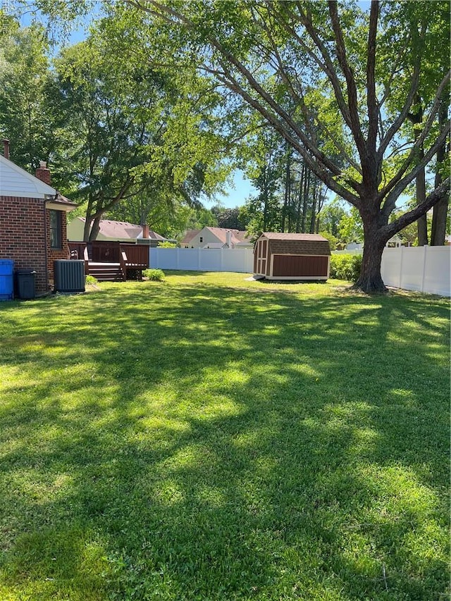 view of yard featuring a fenced backyard, an outdoor structure, central AC, and a storage shed