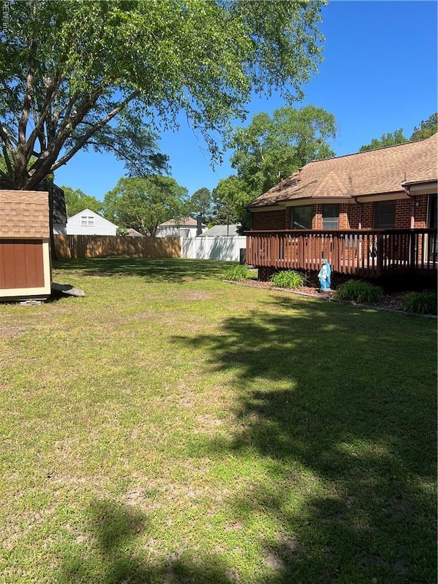 view of yard featuring an outbuilding, a shed, fence, and a wooden deck