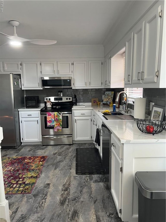 kitchen featuring a sink, stainless steel appliances, white cabinetry, decorative backsplash, and a ceiling fan