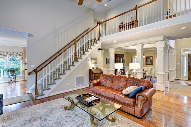 living area featuring wood finished floors, decorative columns, stairs, a towering ceiling, and ceiling fan