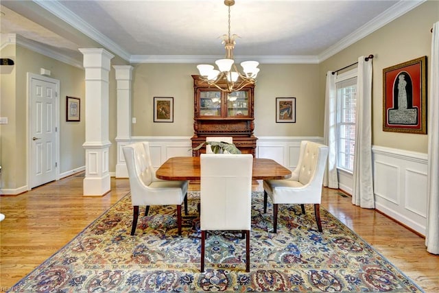dining room with light wood-style floors, a chandelier, ornamental molding, wainscoting, and decorative columns