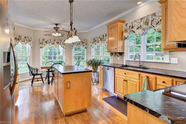 kitchen with a sink, stainless steel appliances, a kitchen island, light wood finished floors, and a ceiling fan