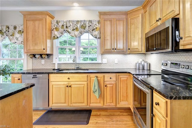 kitchen with stainless steel appliances, a sink, crown molding, backsplash, and dark stone countertops