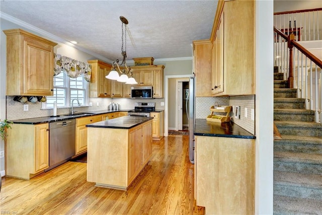 kitchen featuring appliances with stainless steel finishes, a sink, a center island, dark countertops, and light wood-style flooring