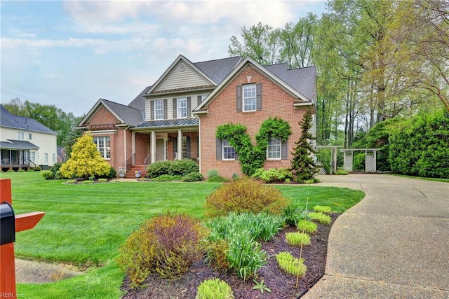 view of front of property featuring a standing seam roof, brick siding, a front yard, and covered porch