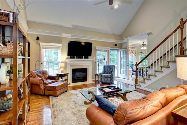 living area with ceiling fan, wood finished floors, a fireplace with flush hearth, stairway, and vaulted ceiling