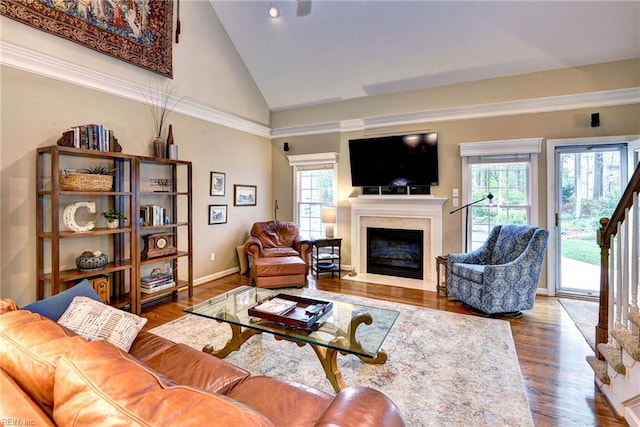 living area featuring healthy amount of natural light, a glass covered fireplace, wood finished floors, high vaulted ceiling, and stairs