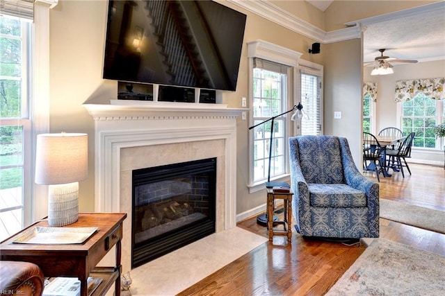 living room with wood finished floors, a high end fireplace, a ceiling fan, crown molding, and baseboards