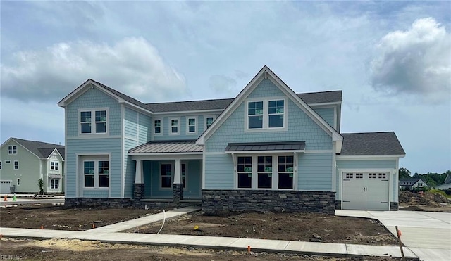 craftsman-style house with a standing seam roof, an attached garage, concrete driveway, stone siding, and a porch