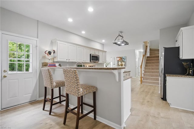 kitchen featuring appliances with stainless steel finishes, a peninsula, a kitchen bar, light wood-type flooring, and white cabinets