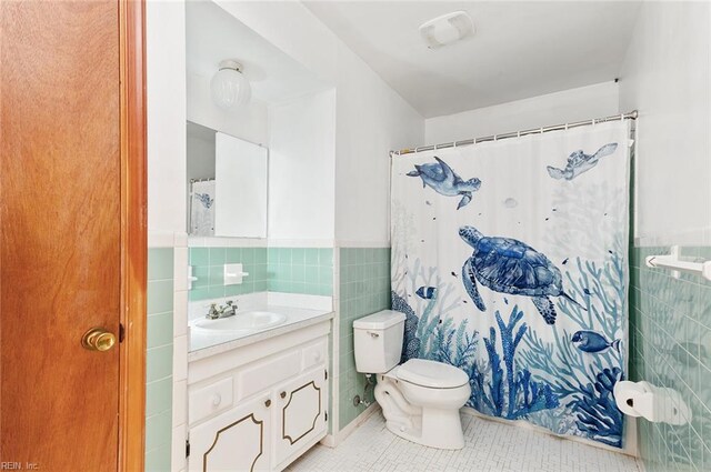 full bath featuring tile walls, tile patterned floors, toilet, a wainscoted wall, and vanity