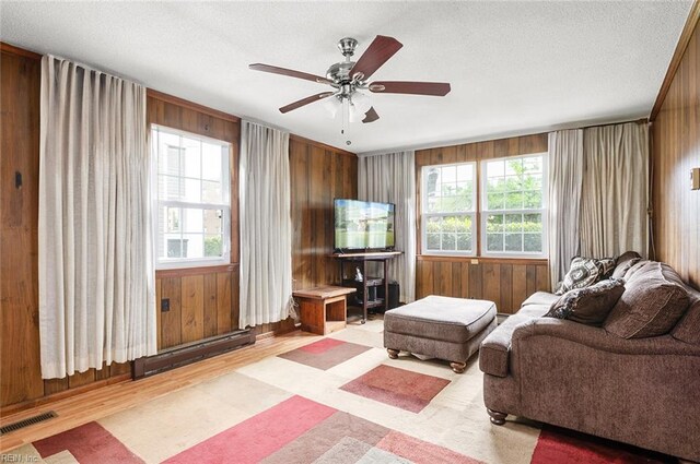 living area with plenty of natural light, a ceiling fan, light wood finished floors, wood walls, and a textured ceiling