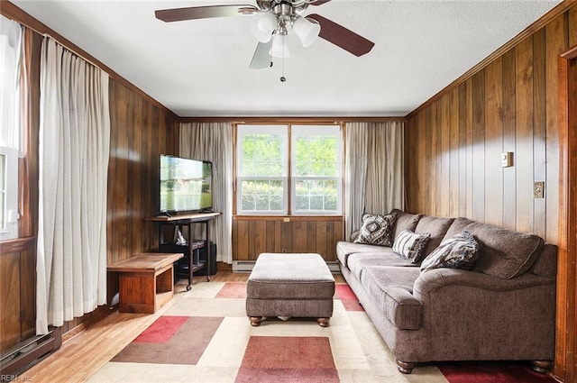 living area featuring wooden walls, ceiling fan, light wood finished floors, a baseboard heating unit, and ornamental molding