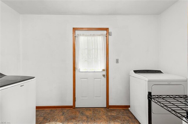 laundry room featuring washing machine and clothes dryer, baseboards, and dark stone finish floors