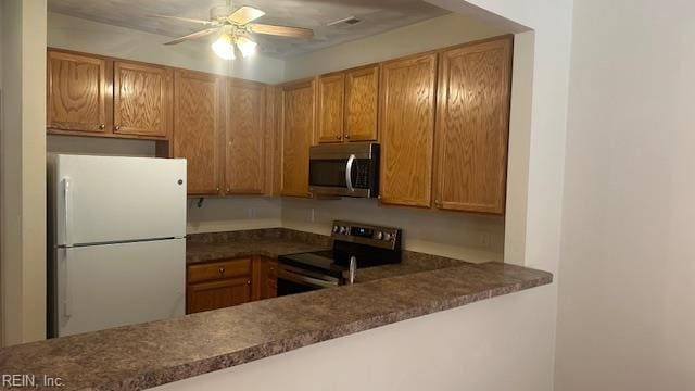 kitchen featuring dark countertops, stainless steel appliances, a ceiling fan, and brown cabinets