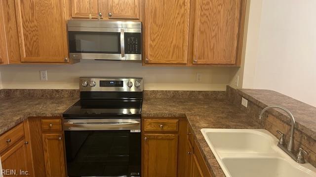 kitchen featuring dark countertops, appliances with stainless steel finishes, brown cabinets, and a sink