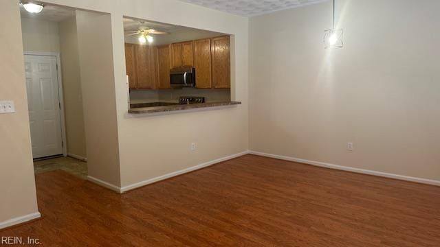 kitchen featuring a ceiling fan, brown cabinets, stainless steel microwave, and wood finished floors