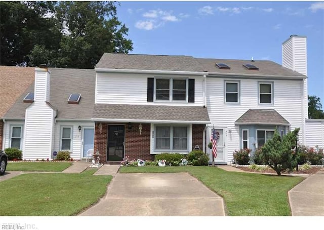 view of front of home with brick siding, roof with shingles, a chimney, and a front yard