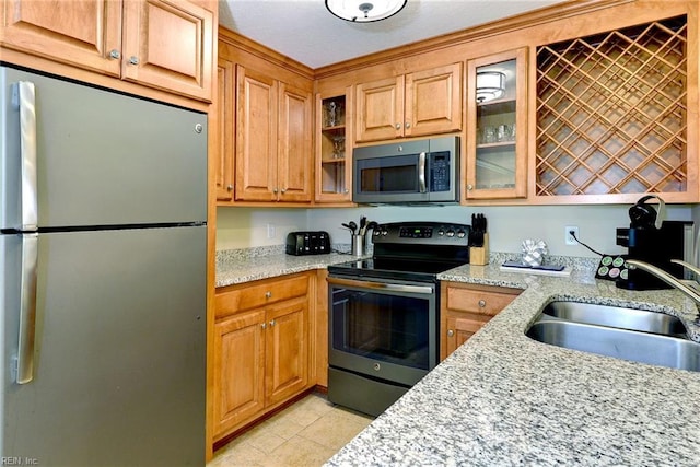 kitchen with glass insert cabinets, a sink, stainless steel appliances, light stone counters, and light tile patterned flooring