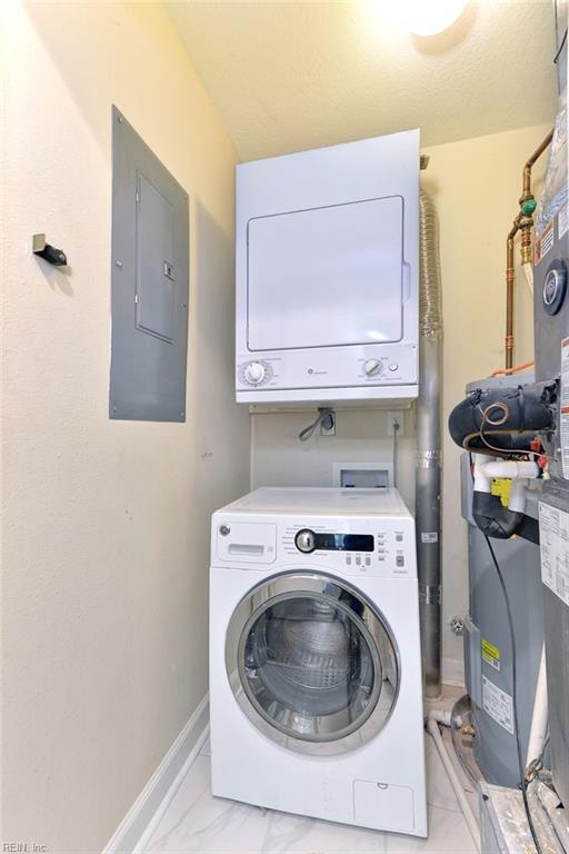washroom with electric panel, marble finish floor, laundry area, stacked washing maching and dryer, and baseboards