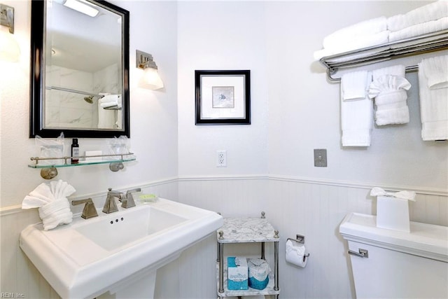 bathroom featuring a sink, toilet, and a wainscoted wall