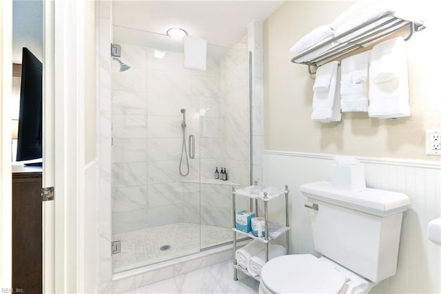 bathroom featuring a stall shower, marble finish floor, toilet, and a wainscoted wall