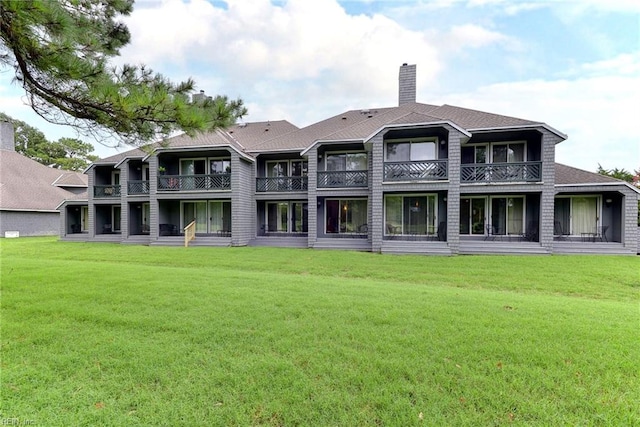 rear view of house featuring a balcony, a chimney, roof with shingles, and a lawn