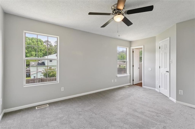unfurnished room featuring a textured ceiling, healthy amount of natural light, carpet flooring, a ceiling fan, and baseboards