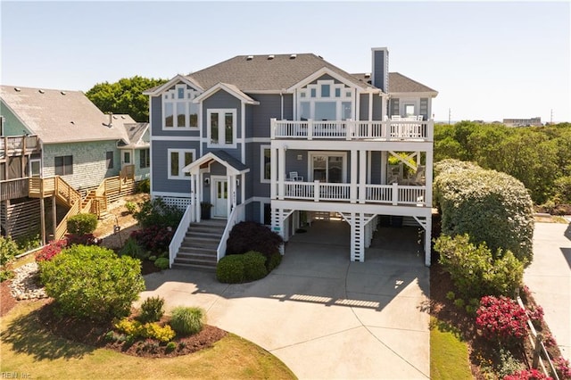 view of front of property featuring a chimney, a carport, a balcony, driveway, and stairs