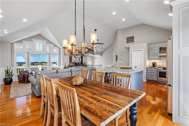 dining space with a notable chandelier, light wood-style flooring, visible vents, and high vaulted ceiling