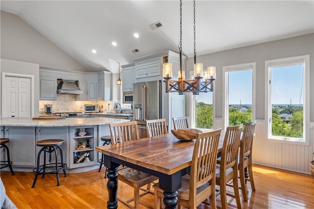 dining space featuring light wood-style flooring, a toaster, visible vents, a chandelier, and vaulted ceiling