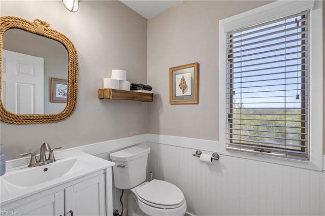 half bathroom featuring vanity, toilet, a wainscoted wall, and plenty of natural light