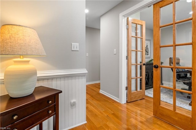 hall featuring light wood-type flooring, french doors, and wainscoting