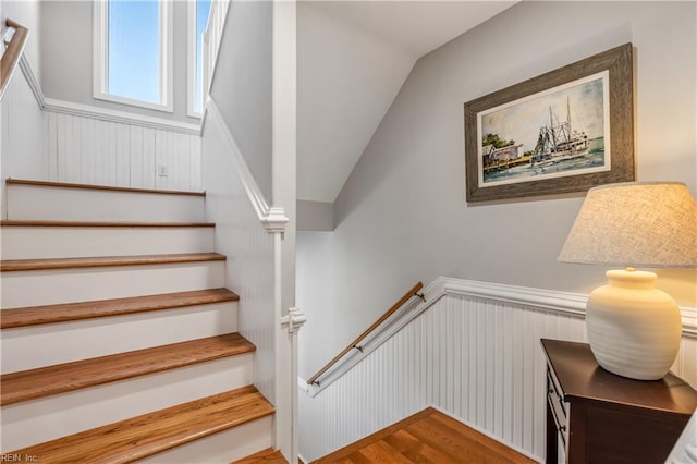 stairs featuring vaulted ceiling, wood finished floors, and wainscoting