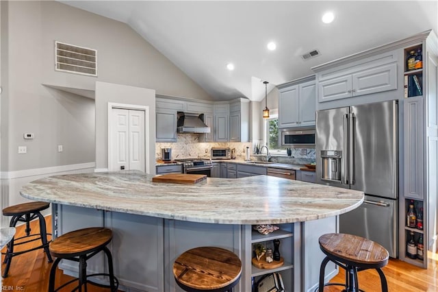 kitchen featuring stainless steel appliances, wall chimney range hood, open shelves, visible vents, and gray cabinetry