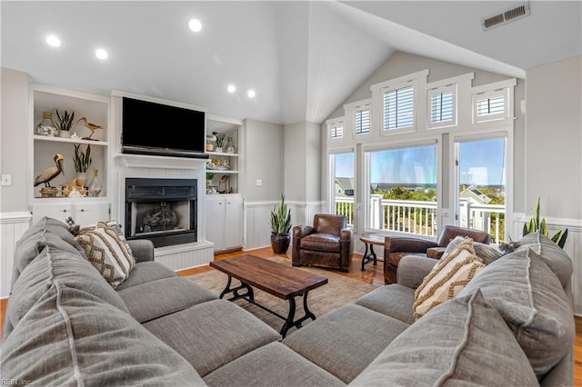 living area featuring a fireplace with raised hearth, visible vents, a wainscoted wall, and wood finished floors