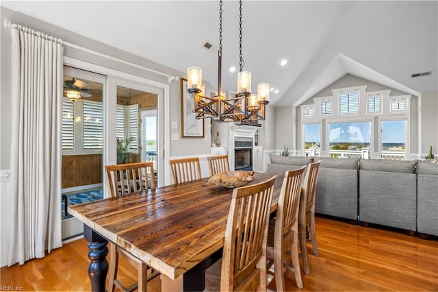 dining room featuring lofted ceiling, light wood finished floors, visible vents, ceiling fan with notable chandelier, and a fireplace