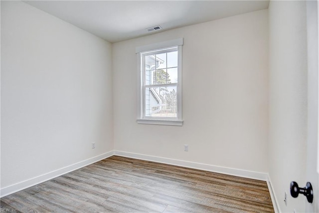 empty room featuring visible vents, wood finished floors, and baseboards