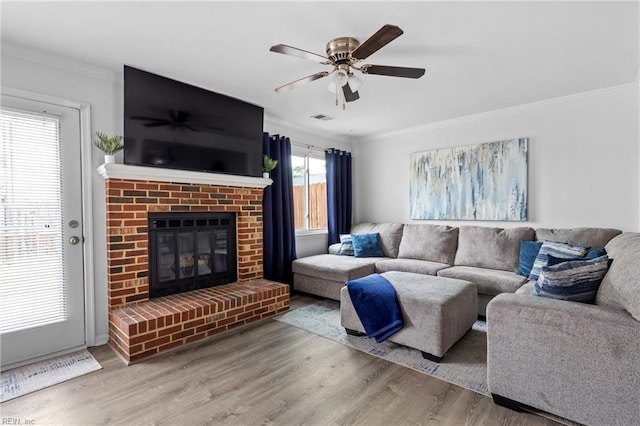 living area with wood finished floors, ornamental molding, a fireplace, and a ceiling fan