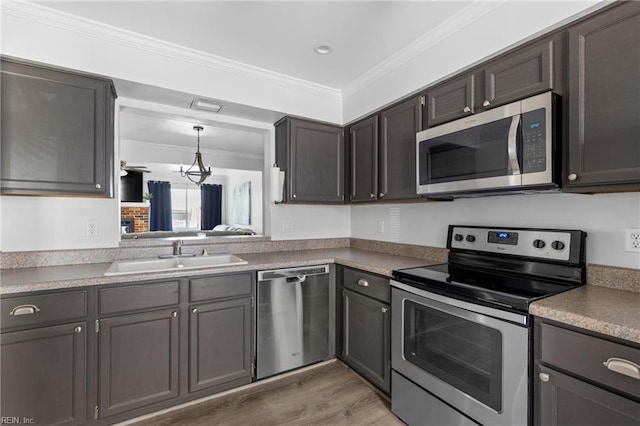 kitchen featuring stainless steel appliances, a sink, crown molding, light wood finished floors, and hanging light fixtures